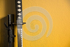 A closeup of Japanese sword katana and scabbard isolated on yellow background wall. Sword used for martial arts such as kenjutsu,