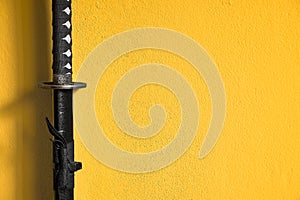 A closeup of Japanese sword katana in scabbard isolated on yellow background wall. Sword used for martial arts such as kenjutsu, photo