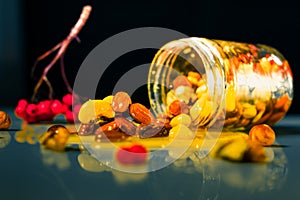 Closeup jar of honey mixed with nuts and rowan berries spilled on a reflective surface on black background