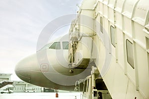 Closeup jet bridge and white airplane parked on airport ground and winter blue sky background