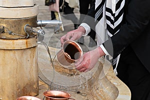 Closeup of a Jewish man using a copper cup for ritual hand washing prior to prayer.