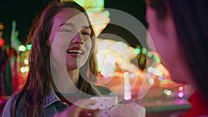 Closeup joyful girl talking friend at illuminated carousel. Happy smiling model