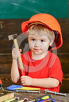 Closeup kid in orange helmet holding hammer in his hands. Crafts lesson at kindergarten. Portrait of little boy in