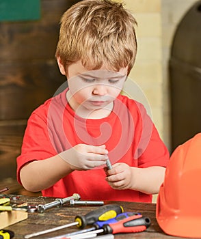 Closeup kid playing with metal bolts. Little laborer in workshop. Cute boy in red T-shirt behind the table