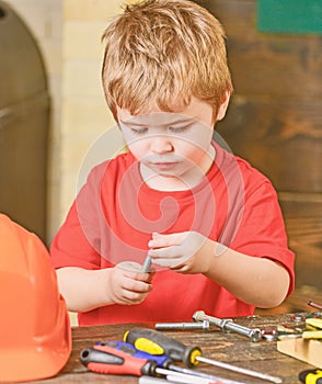 Closeup kid playing with metal bolts. Little laborer in workshop. Cute boy in red T-shirt behind the table