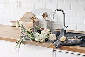 Closeup of kitchen interior. White brick wall, metro tiles, wooden countertops with kitchen utensils. Roses flowers in photo
