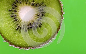 Closeup of a kiwi slice covered in water bubbles against a green background