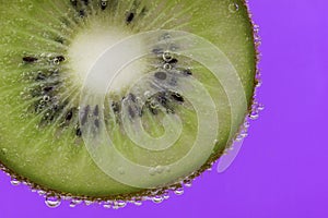 Closeup of a kiwi slice covered in water bubbles against a purple background