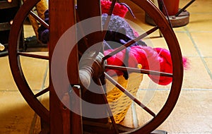 Closeup of knitted colorful purple pink blanket, ball of raw merino wool, knitting needles with old retro wooden spinning wheel