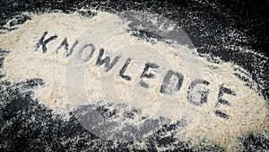 Closeup of KNOWLEDGE text written on white sand