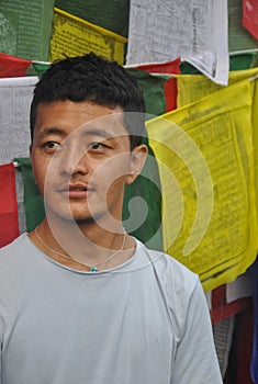 Closeup of a Ladakhi young guy looking sideways, standing against Buddhist prayer flags