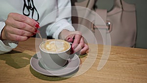 Closeup of a lady stirs the coffee with crema. Woman`s hands and cup cappuccino