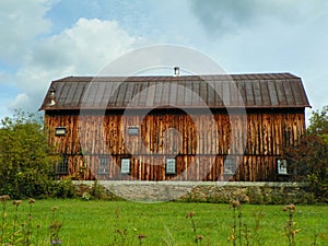 Closeup of large antique cedar wood barn with stone foundation centered in green field.