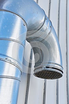 Closeup of a large metal ventilation pipe against the side of a building outside. Engineered stainless steel extractor