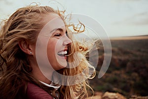 Closeup of a laughing young woman enjoying windy breeze touching face with hair flying while looking away - the feeling