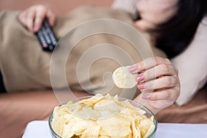 lazy woman eating potato chips lay down on couch and watching tv