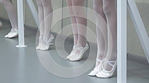 Closeup legs of little ballerinas group in white shoes in row practicing in classical ballet school