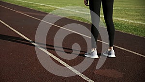 Closeup on legs of sportive female in activewear before jogging on stadium track