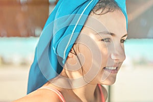 Closeup lifestyle portrait of smiling teen girl with green eyes at the beach with blue towel on the head. Summer