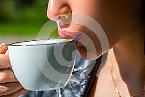 Closeup of the lips of a girl drinking coffee. White mug hot coffee in the hands young girl. Female enjoying aroma