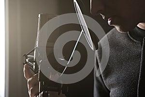 Closeup of lips and hands on a microphone of a young man standing in profile in the rays of the sun