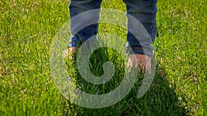Closeup of little baby s feet in jeans standing on green grass lawn. Kids outdoors, children in nature, baby playing outside