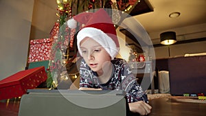 Closeup of little boy celebrating Christmas lying on floor and playing video games on tablet computer. Winter holidays