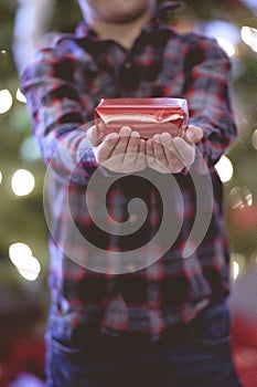 Closeup of a little boy holding a Christmas gift under the lights with a blurry background