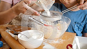 Closeup of little boy with mother sifting flour with sieve. Children cooking with parents, little chef, family having