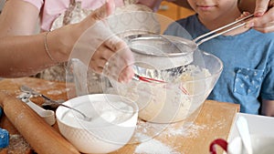 Closeup of little boy with mother sifting flour with sieve. Children cooking with parents, little chef, family having