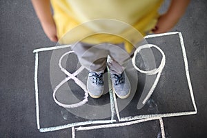 Closeup of little boy`s legs and hopscotch drawn on asphalt. Child playing hopscotch game on playground outdoors on a sunny day