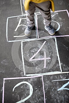 Closeup of little boy`s legs and hopscotch drawn on asphalt. Child playing hopscotch game on playground outdoors on a sunny day