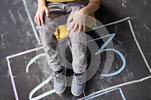 Closeup of little boy`s legs and hopscotch drawn on asphalt. Child playing hopscotch game on playground outdoors on a sunny day