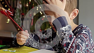 Closeup of little boy thinking of his wishes while writing a letter to Santa on Christmas