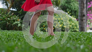 Closeup little girl playing outdoors runs on bright green beautiful grass with yellow flowers, outdoors at high angle