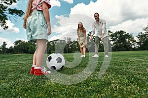 Closeup of little girl ready for kicking the ball. Young family playing football on the grass field in the park on a