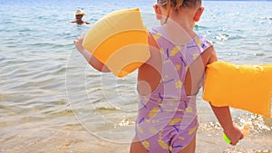 Closeup Little Girl in Safety Armbands Goes to Mother in Sea