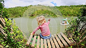 Closeup Little Girl Sits on Bench In Clipped Bush Watches Lake