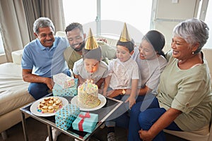 Closeup of a little mixed race boy blowing the candles on a cake at a birthday party with his little brother, parents