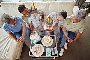 Closeup of a little mixed race boy blowing the candles on a cake at a birthday party with his little brother, parents