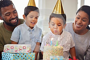 Closeup of a little mixed race boy blowing the candles on a cake at a birthday party with his little brother and parents