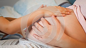 Closeup of little toddler boy stroking and touching big belly of pregnant mother lying in bed