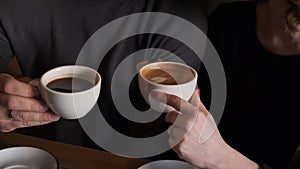 Closeup of loving couple, man and woman drinking coffee from a white ceramic cups, sitting at a table in cafe.