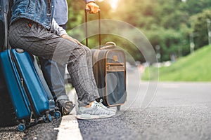 Closeup lower body of Asian couple relaxing on SUV car trunk with yellow trolly luggage along road trip with mountain hill