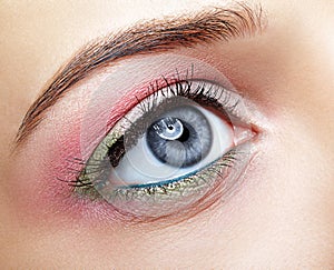 Closeup macro image of human woman eye with pink and green makeup