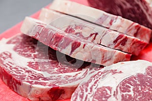 Closeup macro pieces ribeye marbled beef steak on red plastic cutting board on metal table in restaurant kitchen. Concept packing