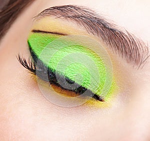 Closeup macro shot of closed human female eye. Girl with green and yellow eyes shadows