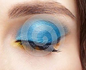 Closed human female eye with blue smoky eyes shadows and yellow liner