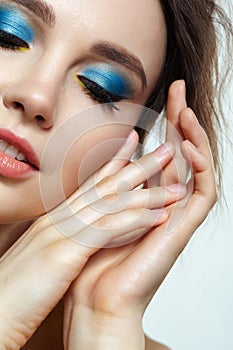 Closeup macro shot of human female face with hands near face, yellow liner and blue eyes shadows makeup