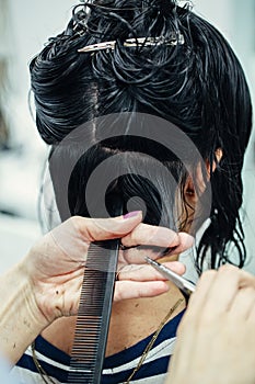 Closeup macro shot image of hairstylist hairdresser cutting customer woman hair in salon with scissors and comb